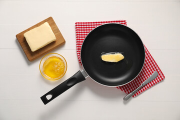 Melting butter in frying pan and knife on white wooden table, flat lay