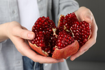 Woman holding fresh pomegranate on grey background, closeup