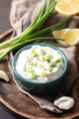 Delicious yogurt in bowl, green onion and spoon on table
