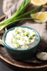 Delicious yogurt in bowl and green onion on table, closeup