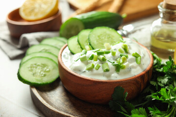 Delicious yogurt with green onion, cucumbers and parsley on light table, closeup