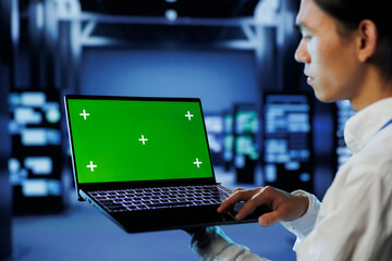 IT consultant with green screen laptop between server hub clusters providing processing resources...