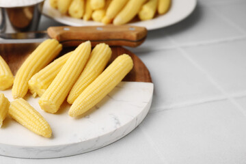 Tasty fresh yellow baby corns and knife on white tiled table, closeup. Space for text