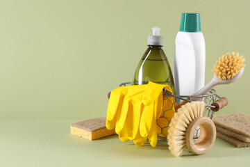 Set of different cleaning supplies in basket on light green background. Space for text