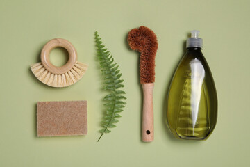 Bottle of cleaning product, brushes, sponge and fern leaf on green background, flat lay