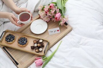 Tasty breakfast served in bed. Woman with tea, desserts, flowers and I Love You card at home, above...