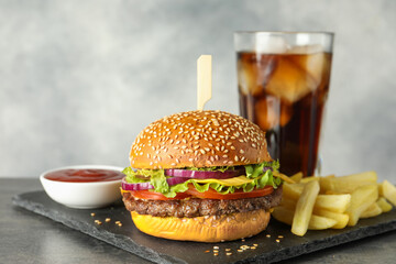 Burger with delicious patty, soda drink, french fries and sauce on dark table against gray...