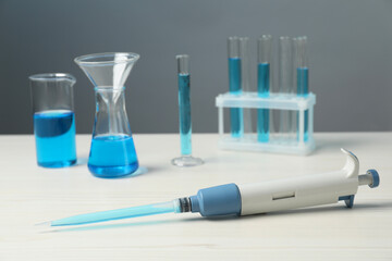 Laboratory analysis. Micropipette and different glassware with liquids on white wooden table