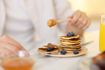 Man pouring honey onto pancakes with blueberries at table, closeup