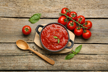 Homemade tomato sauce in bowl, spoon and fresh ingredients on wooden table, flat lay