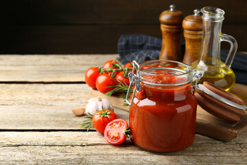 Homemade tomato sauce in jar and ingredients on wooden table, closeup. Space for text