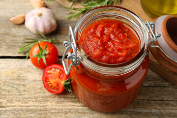 Homemade tomato sauce in jar and fresh ingredients on wooden table, closeup
