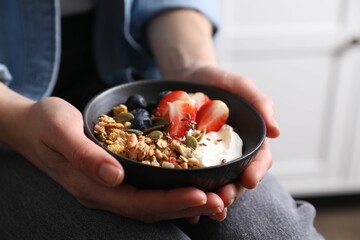 Woman holding bowl of tasty granola with berries, yogurt and seeds indoors, closeup