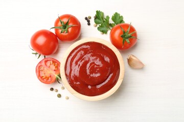 Delicious ketchup in bowl, peppercorns and tomatoes on white wooden table, flat lay