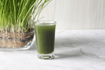 Wheat grass drink in shot glass and fresh sprouts on white marble table, space for text