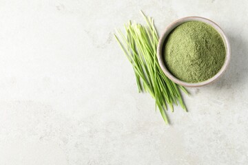 Wheat grass powder in bowl and fresh sprouts on light table, flat lay. Space for text