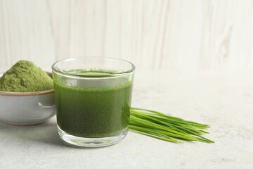 Wheat grass drink in glass, fresh sprouts and bowl of green powder on light table. Space for text