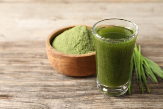 Wheat grass drink in shot glass on wooden table, closeup. Space for text