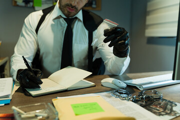 Closeup of a detective wearing gloves and taking notes while examining a piece of evidence
