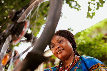 Young sports-loving black woman examining bicycle tire in home yard for damage to repair with...