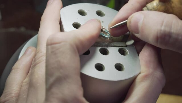 Close shot of goldsmith pushing clasps tighter over turquoise gems in a ring.