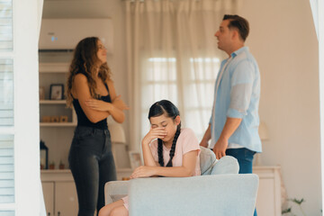Annoyed and unhappy young girl sitting on sofa trapped in middle of tension by her parent argument...