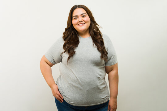 Happy overweight Latin woman standing confidently in a studio while wearing a gray t-shirt for a mockup product shot