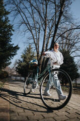 Fototapeta premium A young woman with headphones on smiles broadly while riding a classic bike, enjoying music and sunshine in a serene park setting.