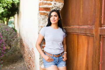 Beautiful latin american woman stands confidently in a casual grey t-shirt and denim shorts outdoors, perfect for a mockup