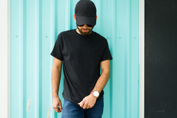 Mockup and casual wear design: hispanic man wearing a black t-shirt and cap against a turquoise...