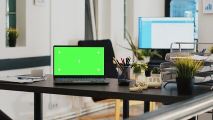 Office with green screen laptop and display in background with scheduled clients list. Mockup notebook in workspace and customers financial consultations list in the back on monitor