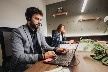 A man and woman working diligently in an office setting, focused on their tasks with computers and office accessories.