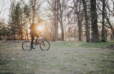 A man enjoys a leisurely bike ride through a scenic park as the sun sets, casting a warm glow and...