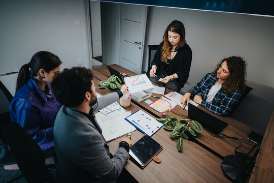 A diverse group of colleagues engaged in a business meeting, collaborating and discussing project strategies using digital and physical tools in a modern office environment.