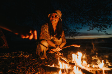 Group of friends gathered around a campfire, cooking food and enjoying the wilderness by a lake at...