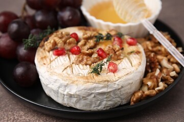 Plate with tasty baked camembert, honey, walnuts and pomegranate seeds on brown table, closeup