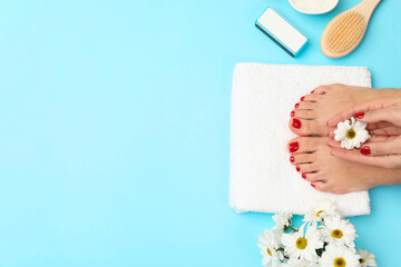 Woman with stylish red toenails after pedicure procedure and chamomile flowers on light blue background, top view. Space for text