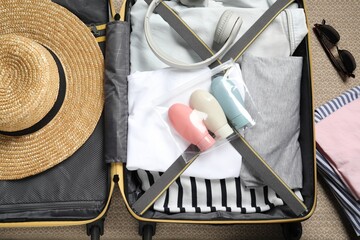 Plastic bag of cosmetic travel kit and clothes in suitcase, top view