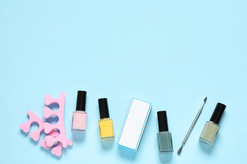 Nail polishes, toe separators, buffer and cuticle pusher on light blue background, flat lay. Space...