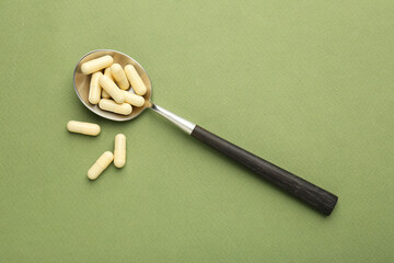 Vitamin capsules in spoon on olive background, top view