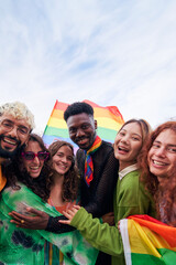 Happy vertical portrait of a group of people celebrating Pride Festival Day with rainbow flags. LGBT community concept. Men and women hugging looking at camera smiling outdoors. Copy space.