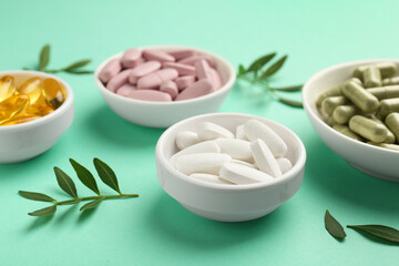 Different vitamin capsules in bowls and leaves on turquoise background, closeup