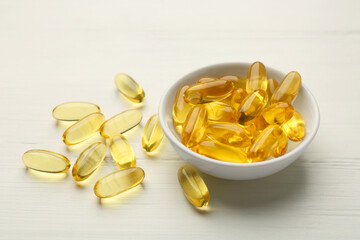 Vitamin capsules in bowl on white wooden table