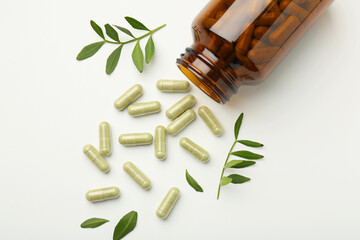 Bottle, vitamin capsules and leaves on white background, flat lay