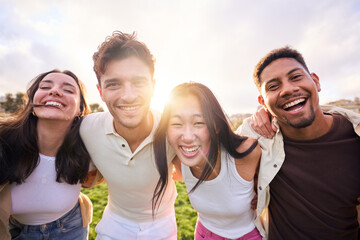 Group of multirracial young people smiling at camera outside. Cheerful community of university students standing in college campus. Team building concept with guys and girls hugging together.