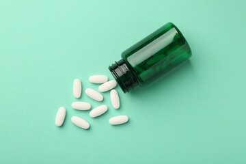Vitamin pills and bottle on mint color background, top view