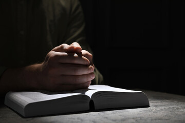 Religion. Christian man praying over Bible at table, closeup. Space for text