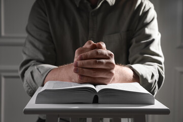 Religion. Christian man praying over Bible indoors, closeup