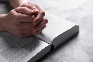 Religion. Christian woman praying over Bible at gray textured table, closeup