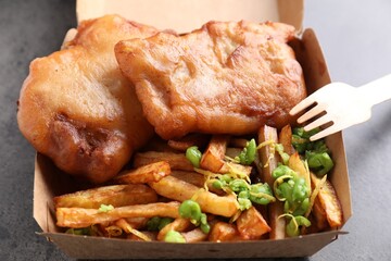 Tasty fish, chips and peas in paper box on grey table, above view